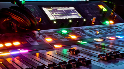 Low angle close up on a dark studio mixing sound board, with rows of small dials illuminated by a...