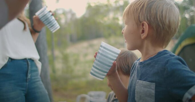 family is resting at nature, campsite in forest with tent, little boys are drinking water, summer vacation