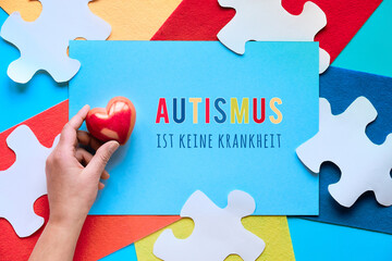 German text means Autism is not a disease. Jigsaw puzzle element on layered felt pieces, top view.