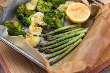 Baked asparagus, broccoli and cauliflower with spices and lemon on parchment paper close up. Vegan healthy diet dish