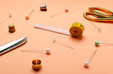 Closeup of lot of sewing pins, thimbles, measuring tape and scissors on the orange desk