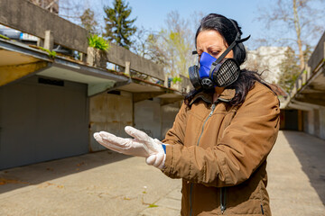 Woman puts gloves on her hands as wearing filter mask