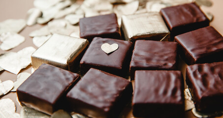 Wrapped and unwrapped square chocolate candy among the foil-cut hearts in close-up. The concept of Valentine's day
