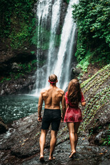 Tourists at the waterfall, rear view. Couple on vacation in Bali. Honeymoon trip. A couple in love travels the world. Vacation on the island of Bali. Tourists in Bali. Copy space
