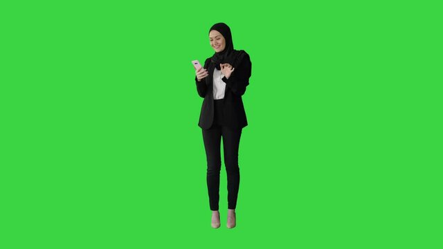 Smiling Arab woman in hijab taking selfie pictures on her mobile phone on a Green Screen, Chroma Key.