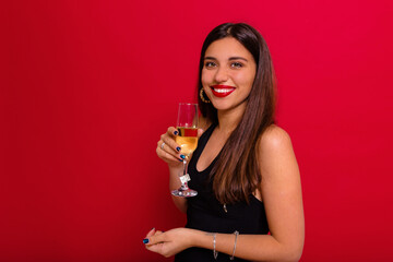 Happy pretty lady dressed black shirt with red lips is posing at camera with a glass of champagne over red background