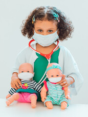 A girl who plays doctor
with two baby dolls as a patient, they all wear protective masks