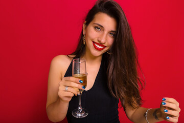 Joyful pretty woman in elegant black dress with champagne celebrating new year, birthday, having fun. Positive emotions, red lips, red background