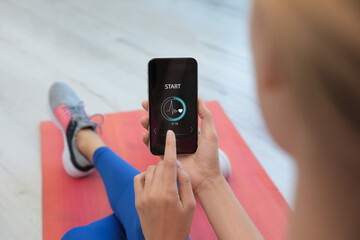 Young woman using fitness app on smartphone indoors, closeup