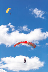 tandem skydiving in the clouds. landing. colorful parachute on the blue sky background