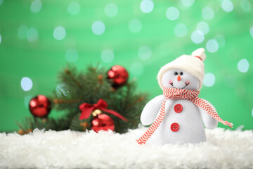 Snowman toy on snow against blurred festive lights, space for text. Christmas decoration