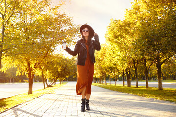 Fototapeta premium Beautiful young woman with cup of coffee wearing stylish clothes in autumn park