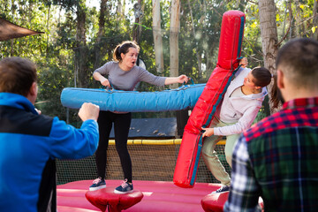 Fototapeta na wymiar Happy female friends fighting by inflatable logs on adults bouncy playground outdoor