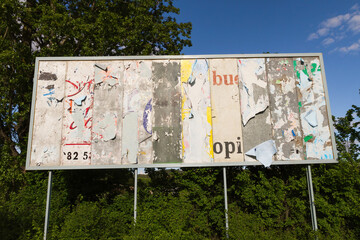 Billboard with torn advertising remains peeled off and deteriorated 