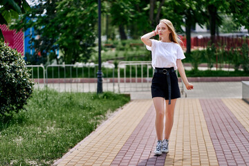 A woman in a black skirt and white t-shirt straightens her hair while walking on nature.