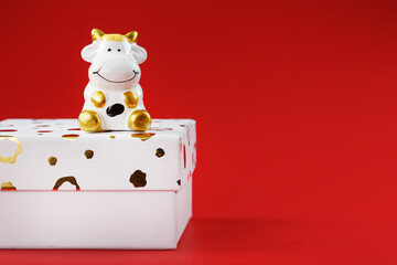 New year's toy of a cow on a box with a gift on a red background. 2021 year of the Bull, cow.