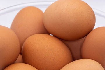 close up of raw brown eggs in a glass bowl against a plain white background