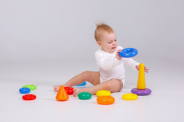 Fototapeta na wymiar baby girl playing with colorful rainbow toy pyramid sitting on floor
