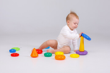 Fototapeta na wymiar baby girl playing with colorful rainbow toy pyramid sitting on floor