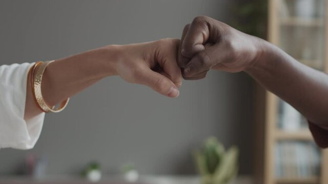 Close up of two diverse unrecognizable businesspeople bumping their fists thus greeting each other in office