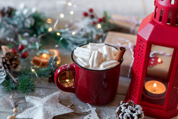 Winter hot drink, cacao with marshmallows and cinnamon or spicy hot chocolate in red cup and Christmas garland. Festive vintage background.