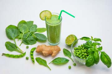 Smoothie in a glass and ingredients - green peas, ginger, basil and spinach leaves on a white background. Healthy vegan cocktail.