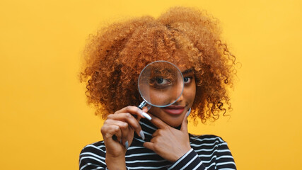 Funny young african american black woman with magnifier in hand shows eye through magnifying glass....