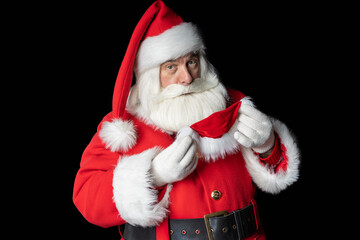 Santa Claus looks and tries on a mask. Black background.