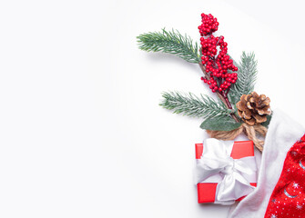 Christmas background on white: fir branch with a cone and berries and red gift box with white ribbon in the Santa Claus hat, space for text, Christmas with space for text