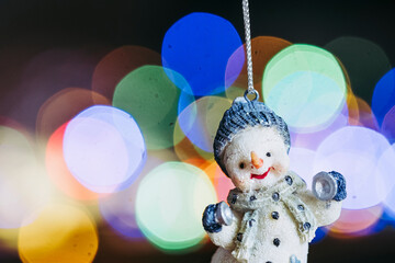 Fototapeta premium Décoration de Noël en forme de bonhomme de neige mignon sur un fond flou coloré - Décor de Noël et bokeh tâches de lumière colorées 