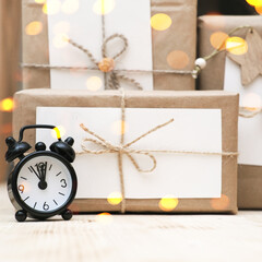 hand made christmas gifts wrapped in craft paper and alarm clock. bokeh lights. christrmas celebration time. sustainable holiday gifts.