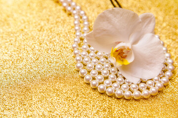 white Orchid and pearl necklace on a shiny gold background
