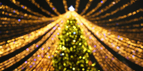 Defocused fur tree with fortuna gold Christmas lights and festive decor at night. Flickering garlands outside, on city's streets. Happy New Year colorful glowing background.  