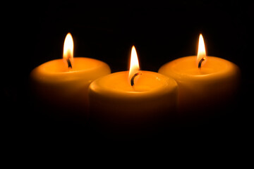 Three large white candles burn in the dark