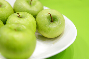 Green apples on a white plate and green background