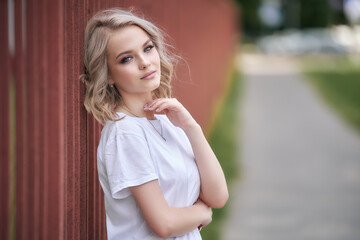 A blond woman in a white T-shirt is leaning on the fence while standing on the path.