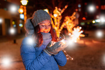 Happy woman with a garland in the winter on the street with festive lighting, Christmas evening