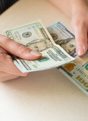 Woman's hands counting dollar bills, on white desk.