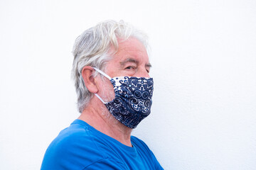 Close-up portrait of a serious senior man with blue t-shirt and coronavirus protective mask as he looks sideways at the camera.