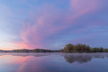 Landscape at dawn of the foggy, spring shoreline of Whitford Lake with reflections in calm water, Fort Custer State Park, Michigan, USA