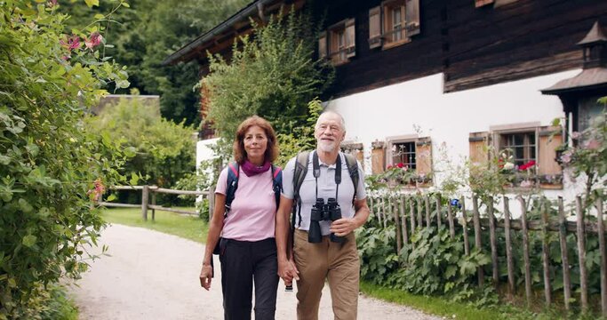 A senior pensioner couple with binoculars hiking,holding hands.