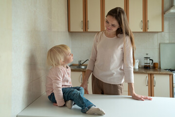 Smiling mother looking at little daughter at table in kitchen. Morning breakfast