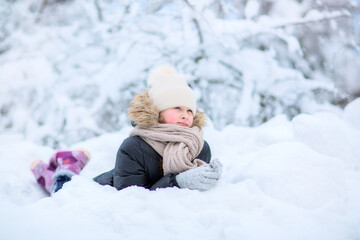  The girl lies in the snow and dreams,  looking into the distance.Background of snow-covered trees