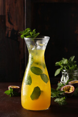 Lemonade. Drink with passion fruit, mint and soda in a clear jug with ice on a brown table with mint. Bar menu. Background image, copy space, vertical