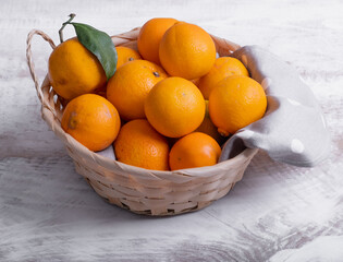 Ripe tangerines stacked in a basket on a white wood background.