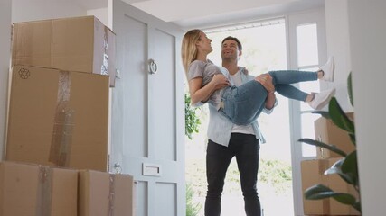 Man carrying woman over threshold and she kisses him as couple move into new home on moving day - shot in slow motion - Powered by Adobe