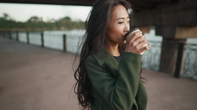 Pretty asian woman drinking coffee enjoy her walk on river embankment. 