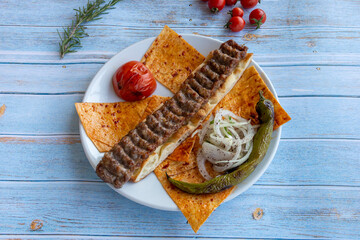 Adana kebab - turkish kebab - with roasted tomatoes, onions and peppers on blue wooden background