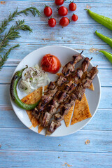 Lamb shish kebab on blue wooden background - with roasted tomatoes, onions and peppers