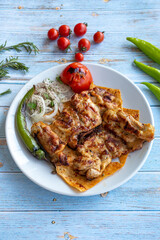 Baked chicken cutlet on blue wood background - with roasted tomatoes, onions and peppers